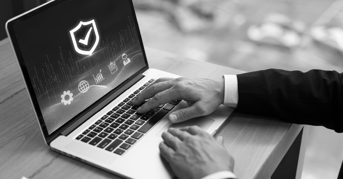 Pessoa utilizando notebook com ícones digitais de segurança e nuvem. Imagem em preto e branco.