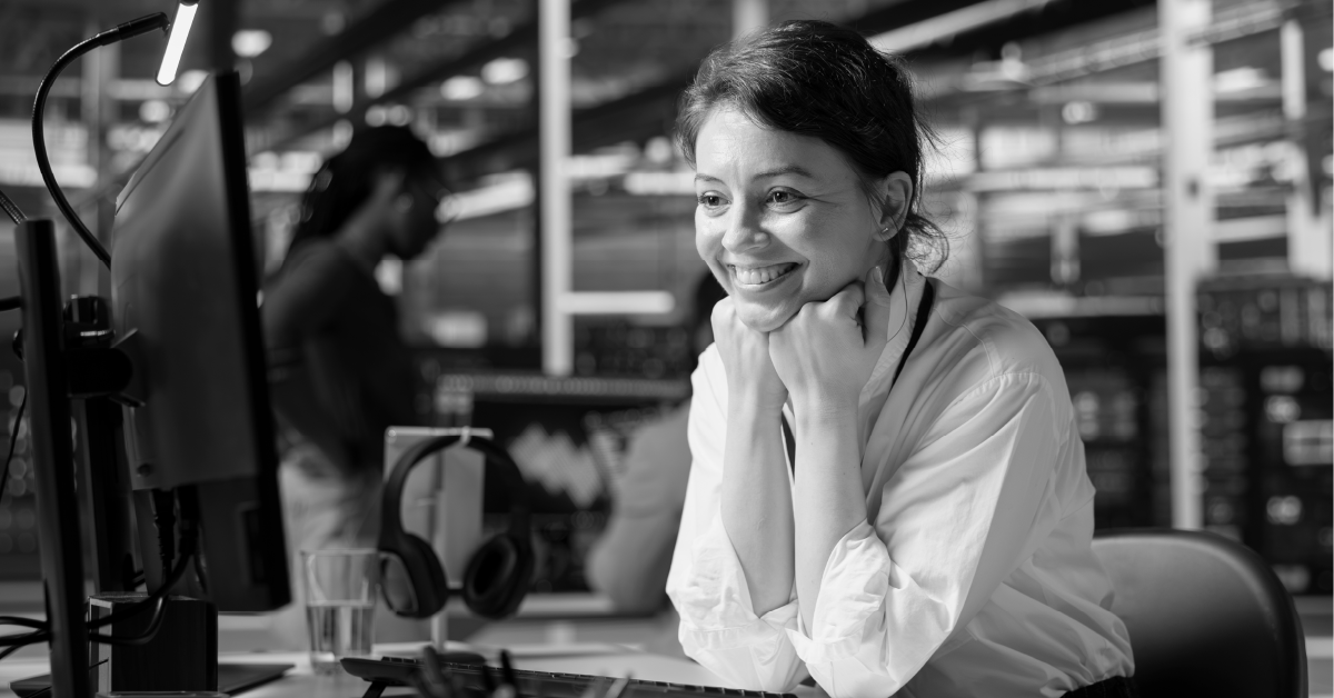 Mulher sorrindo para um computador. Imagem em preto e branco.