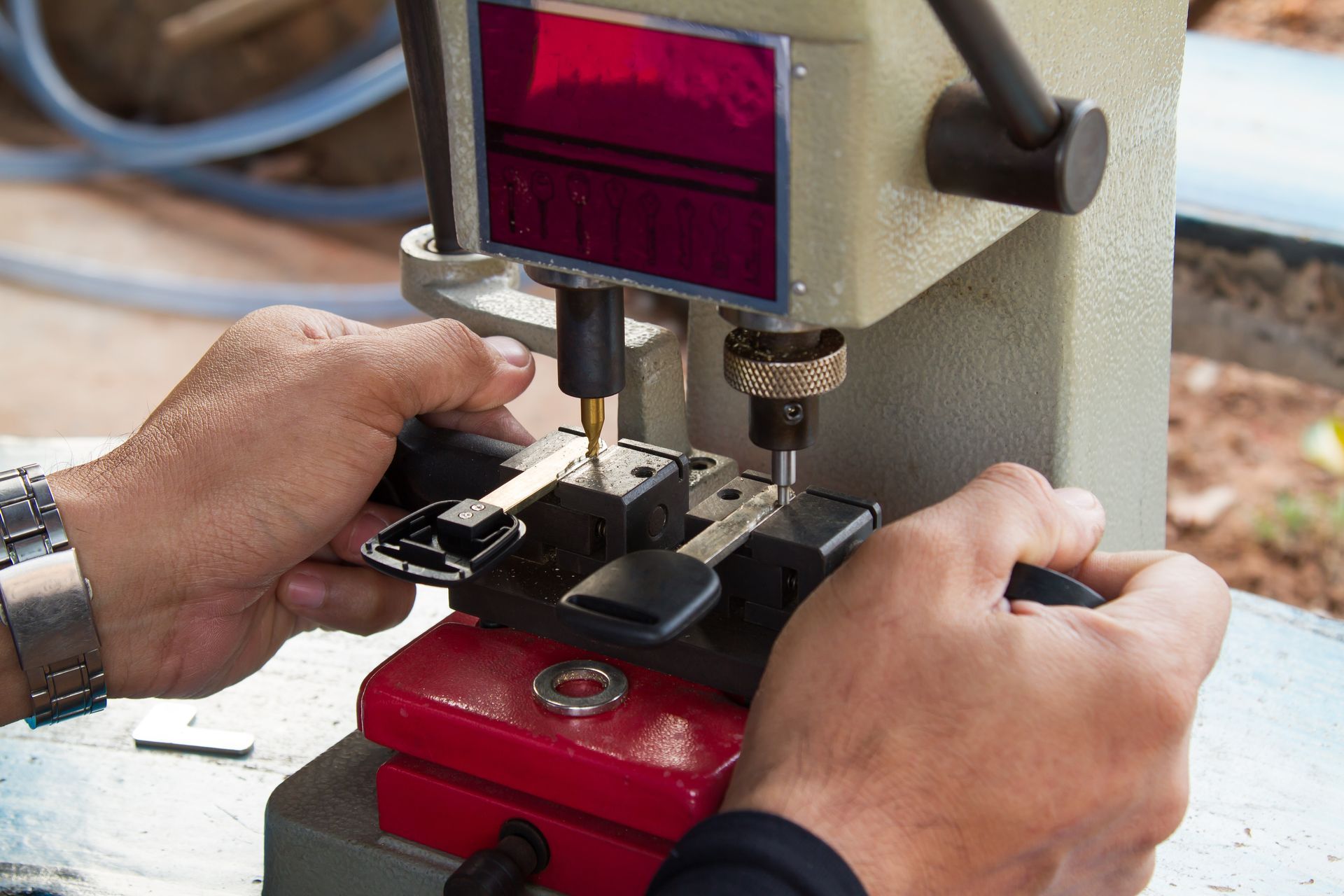 Hands using a key duplicating machine to cut a new key; the machine is gray and red.