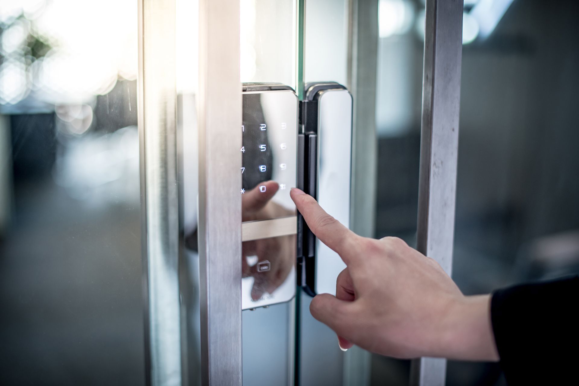 Person's finger touching a digital keypad lock on a glass door.
