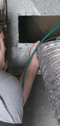 A man is working on a duct with a blue hose.