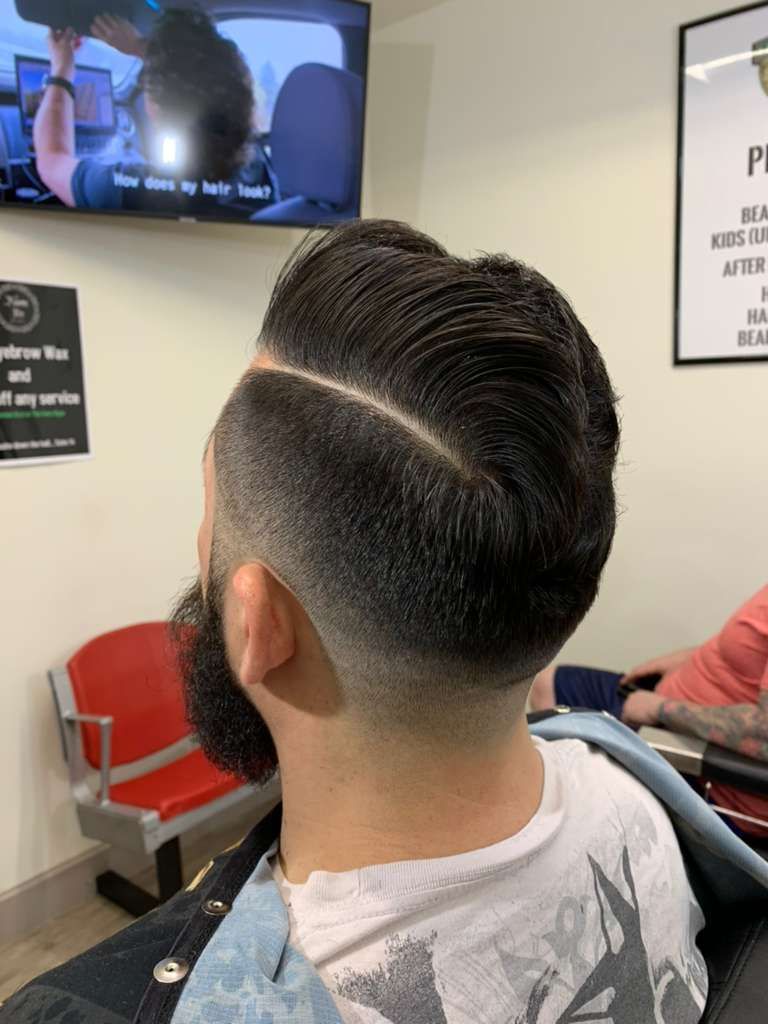Man in barber chair with a dark, side-parted hairstyle and faded sides.