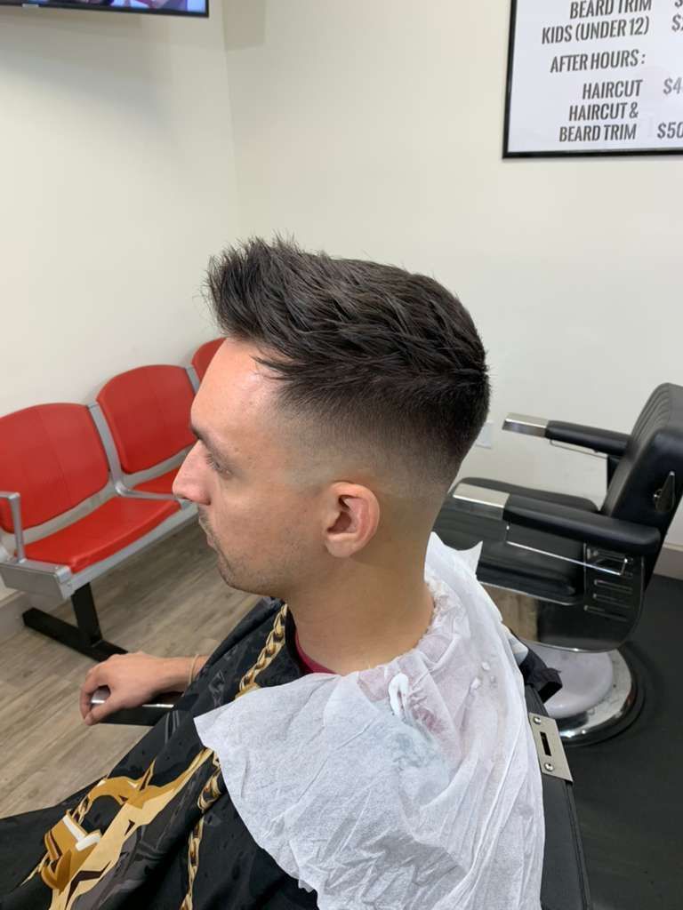 Man in barber chair with faded haircut, spiky top; white paper neck wrap.