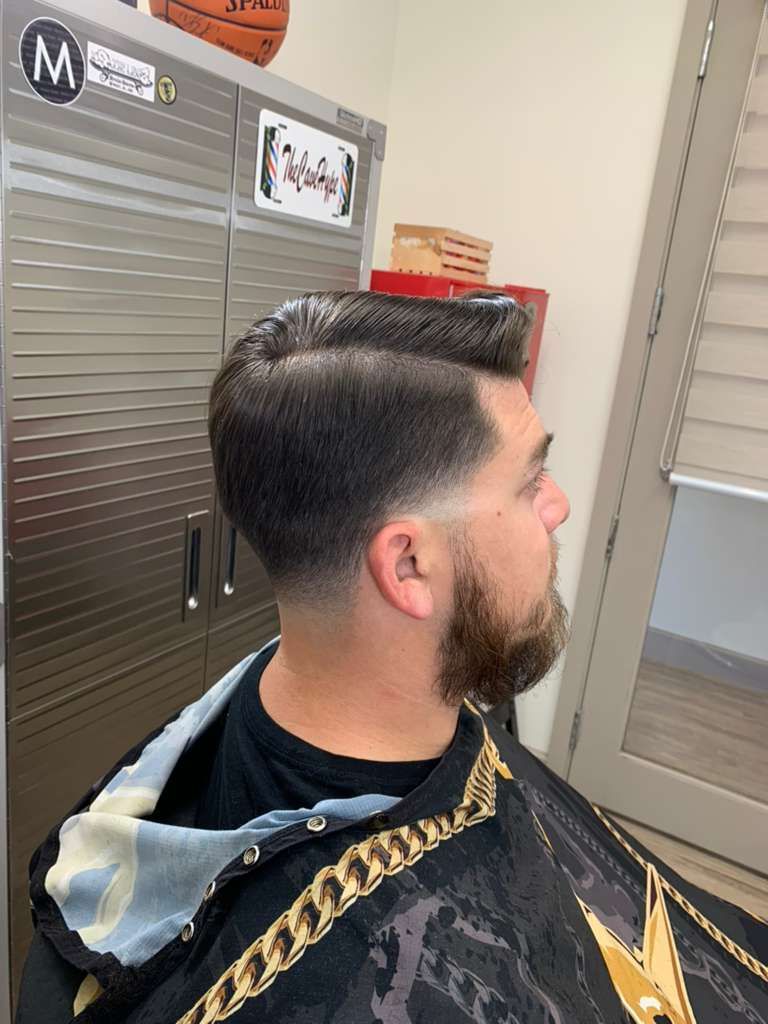 Man with a fade haircut and beard at a barbershop. He is wearing a black cape.