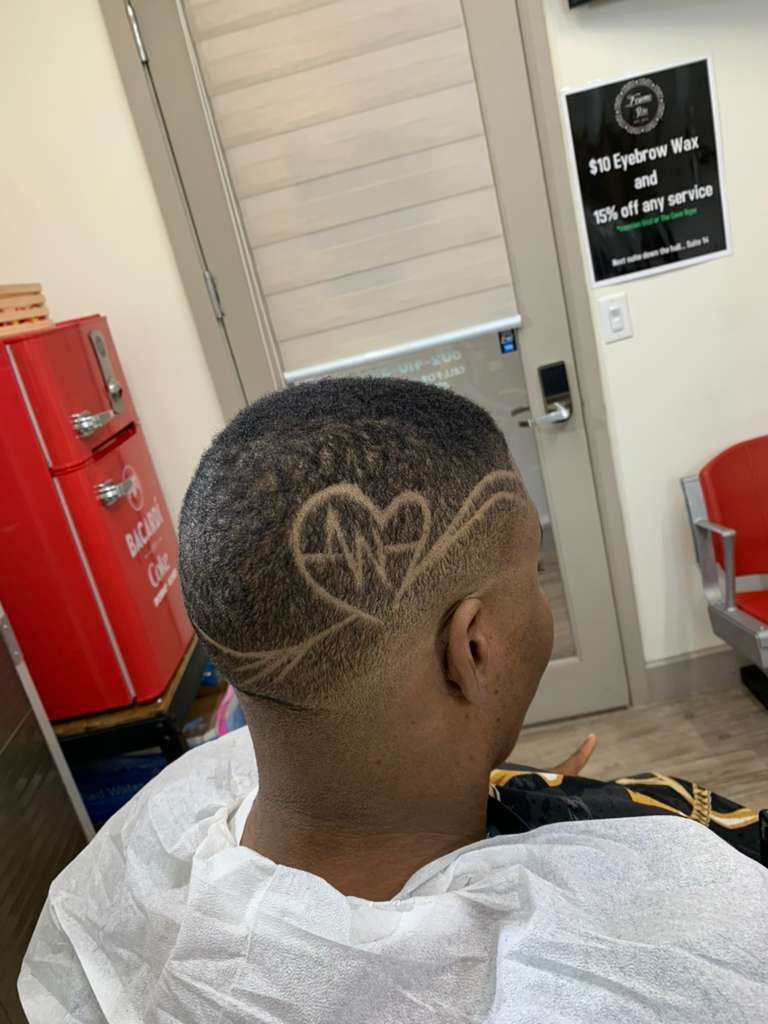 Person in barber chair with a shaved head design of a heartbeat and heart symbol.