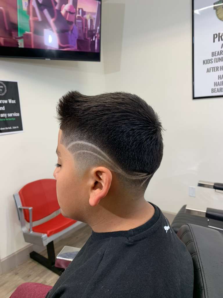 Boy with a fade haircut and design sitting in a barber shop, side view.