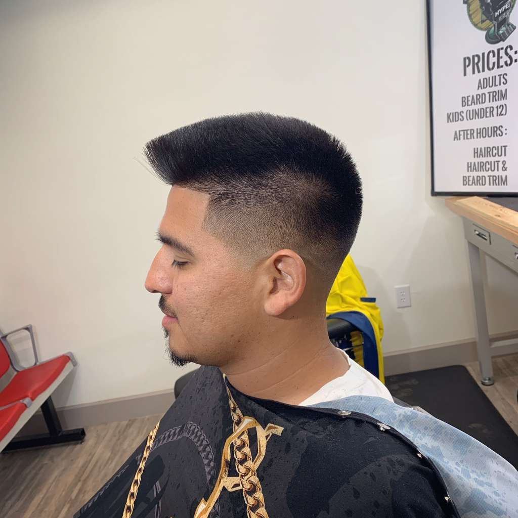 Man with a high-top fade haircut, sitting in a barbershop. He's wearing a black robe.