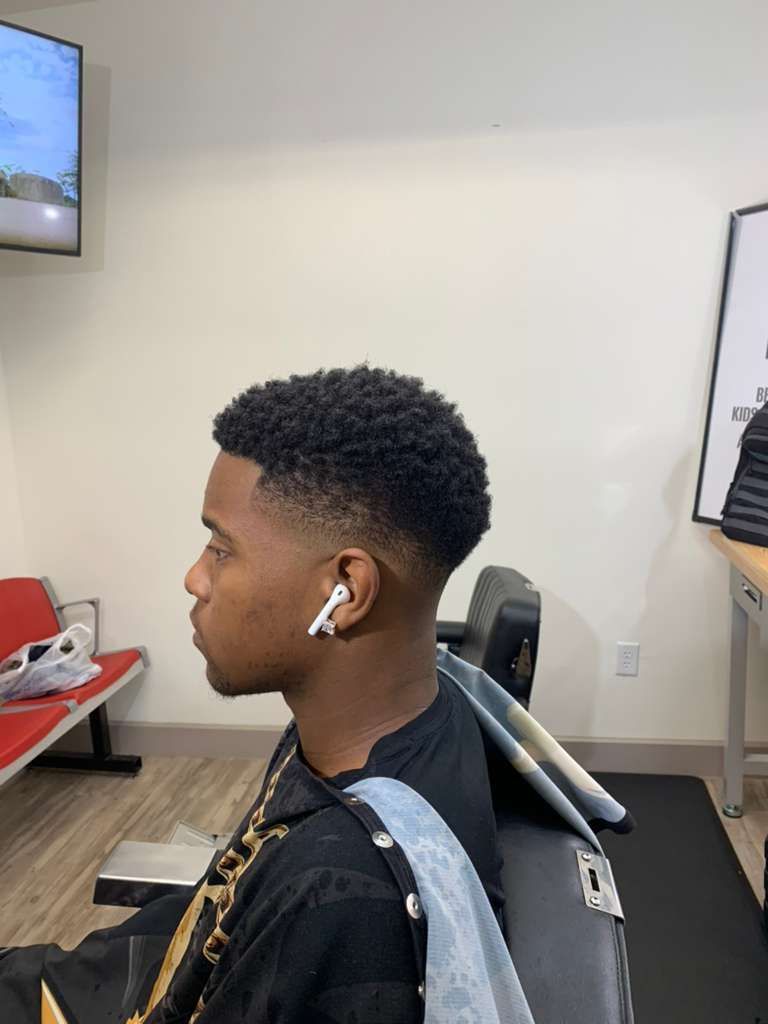 Man with a tapered haircut, wearing earbuds, sitting in a barber chair.