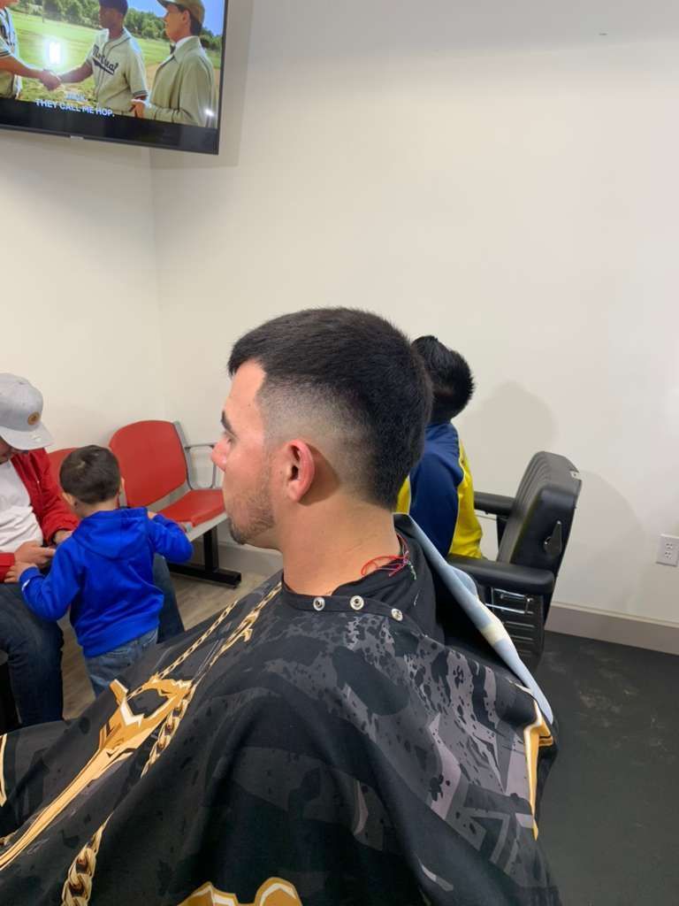 Man getting a haircut at a barber shop, with a low fade. People and TV in the background.