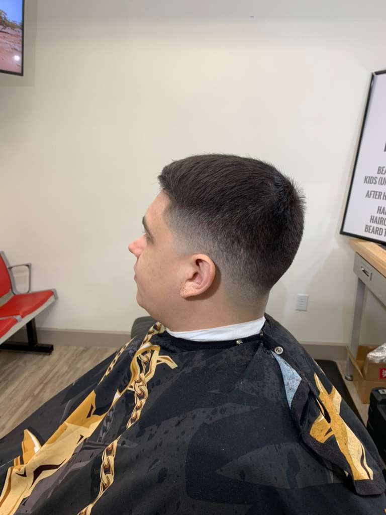 Man with a fade haircut in a barbershop. He is wearing a cape.