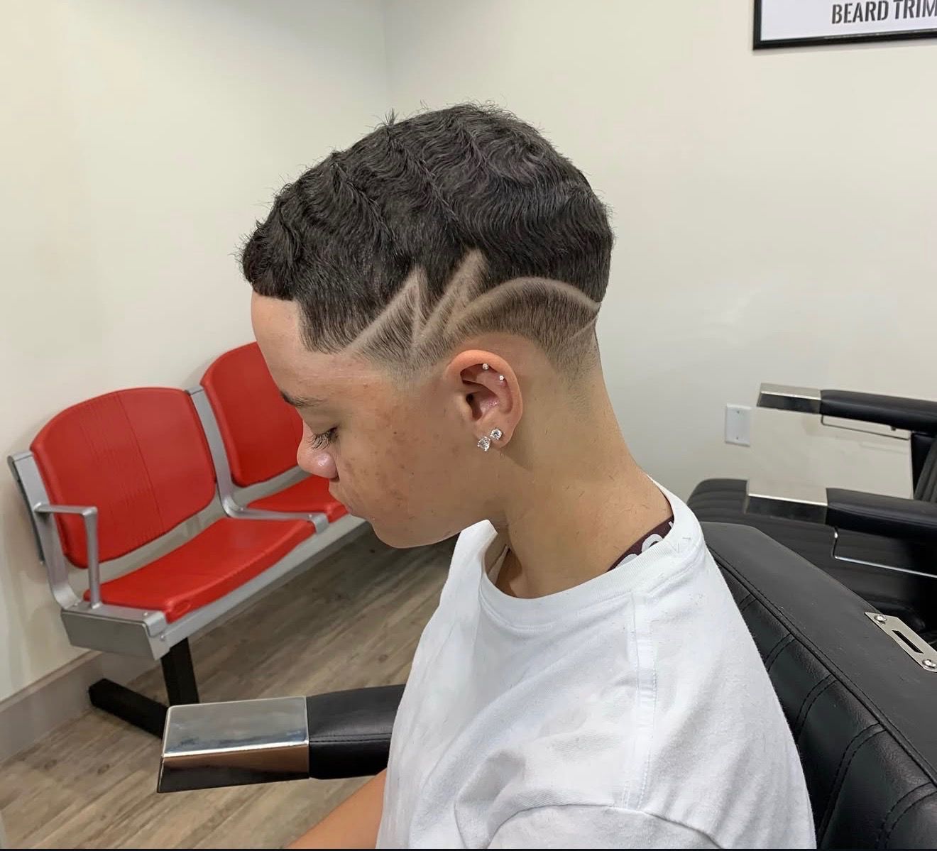 Person with a short haircut featuring a design cut into the side and back. The person is in a barber shop.