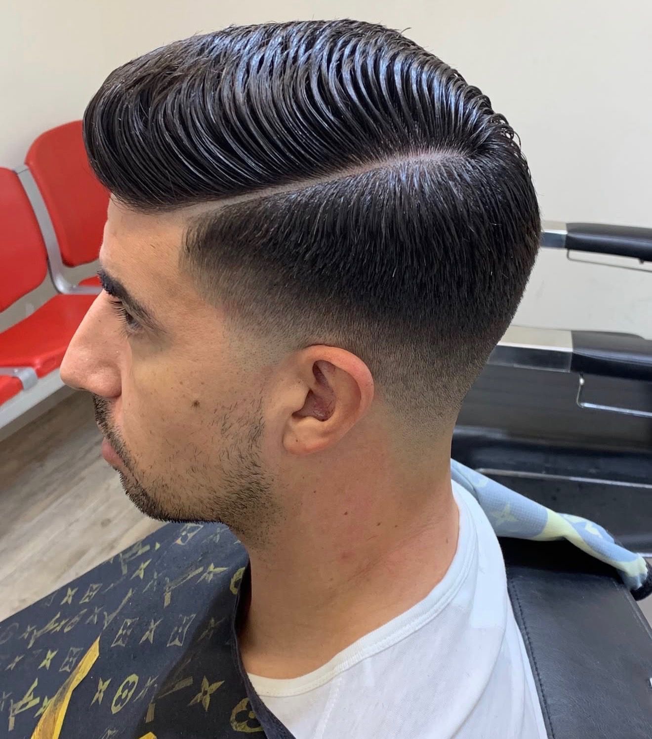 Man with a side-parted hairstyle and a skin fade haircut in a barbershop setting.