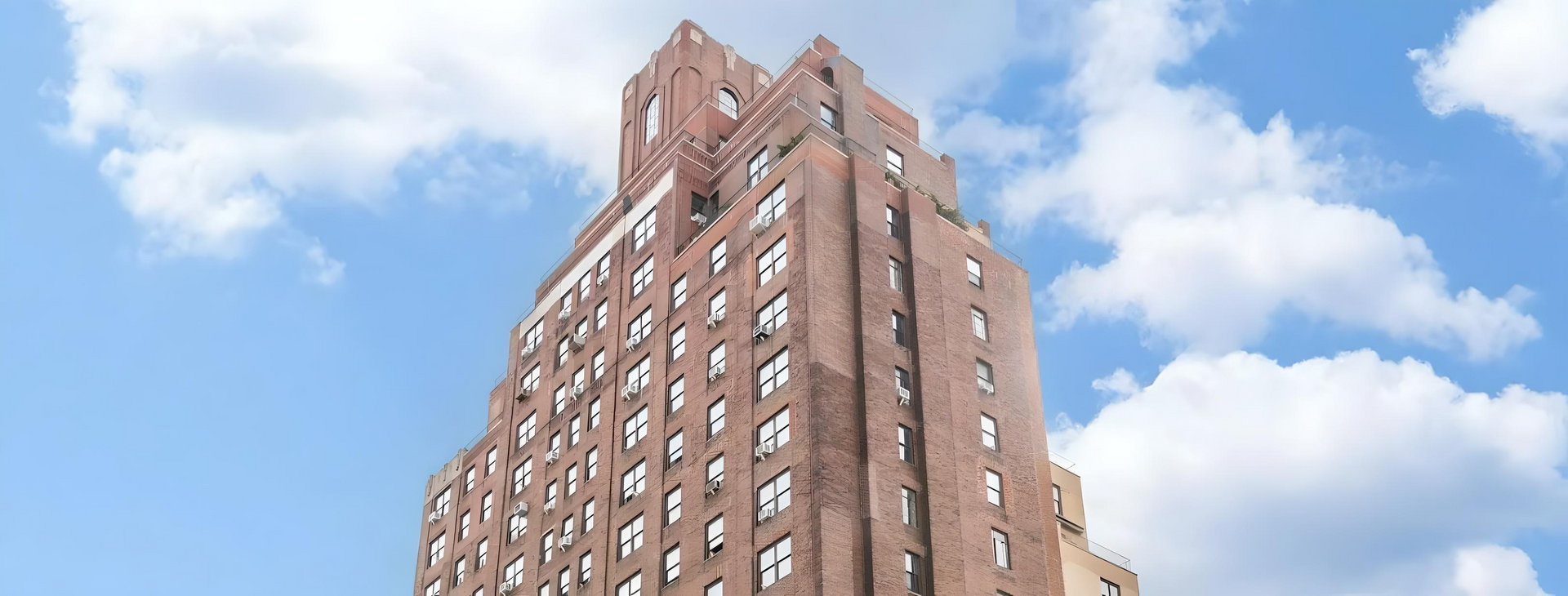 A tall brick building with a blue sky and clouds in the background.