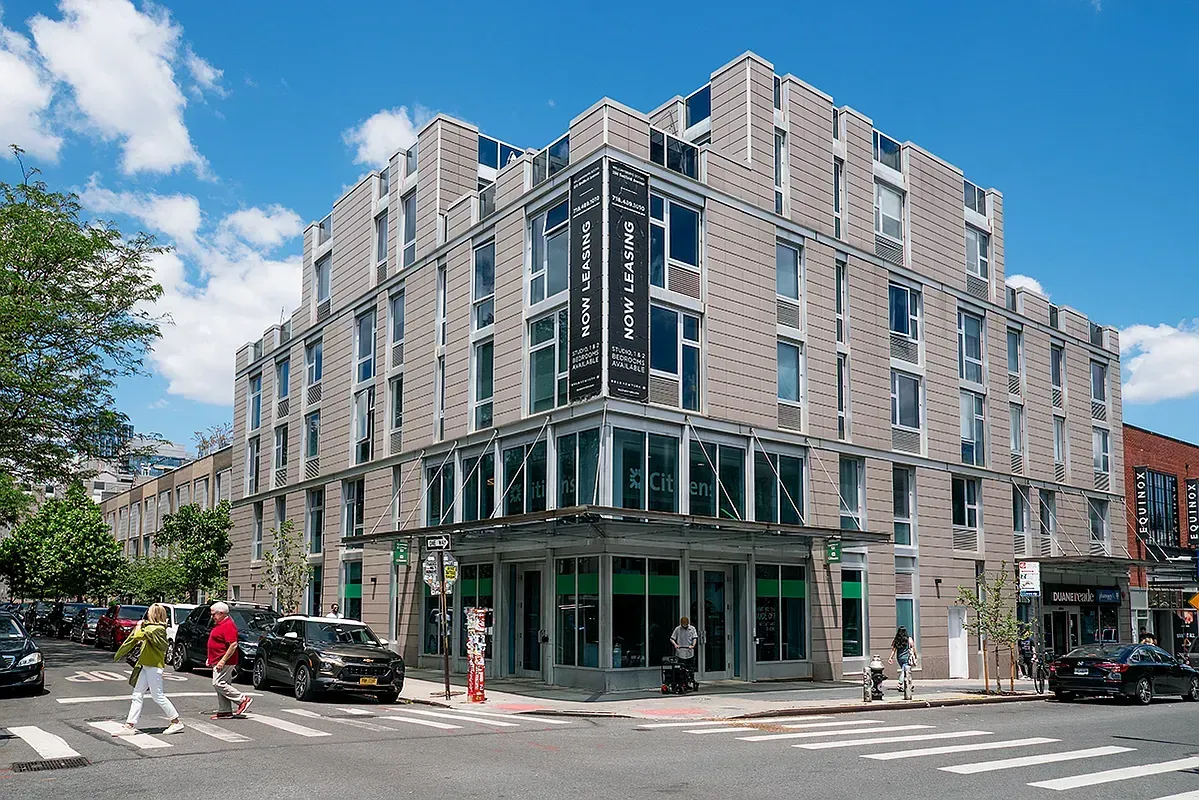 A large building with a lot of windows is on the corner of a city street.