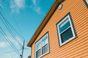Orange house siding with white-trimmed windows under a blue sky, viewed from below