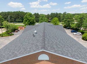 Aerial view of a gray-shingled roof over a brick building, surrounded by trees and a parking lot.