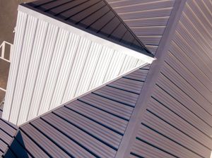 Close-up of a metal roof with a triangular white vent against brown shingles.