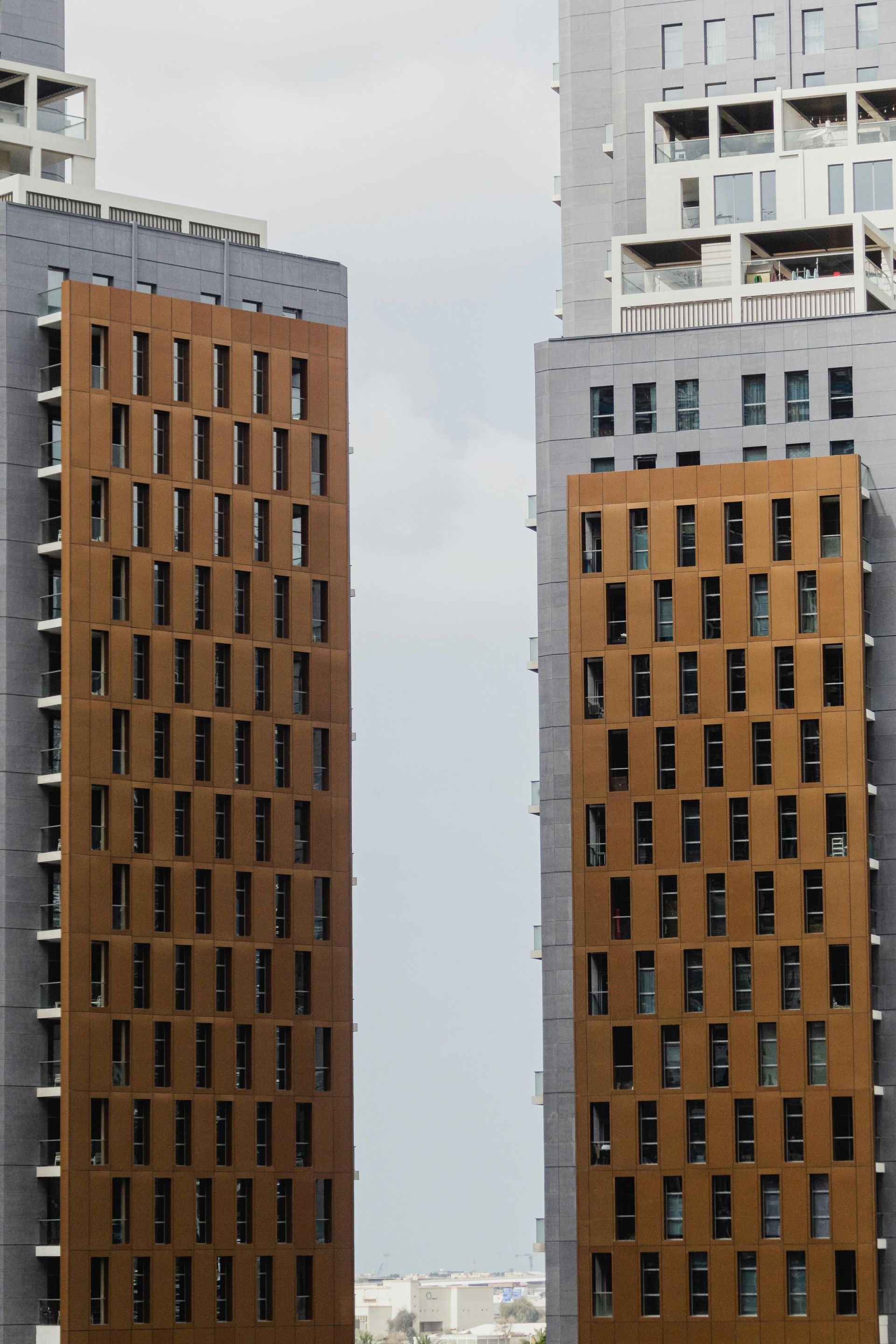 Two modern high-rise buildings with textured brown panels and rectangular windows against a cloudy sky.
