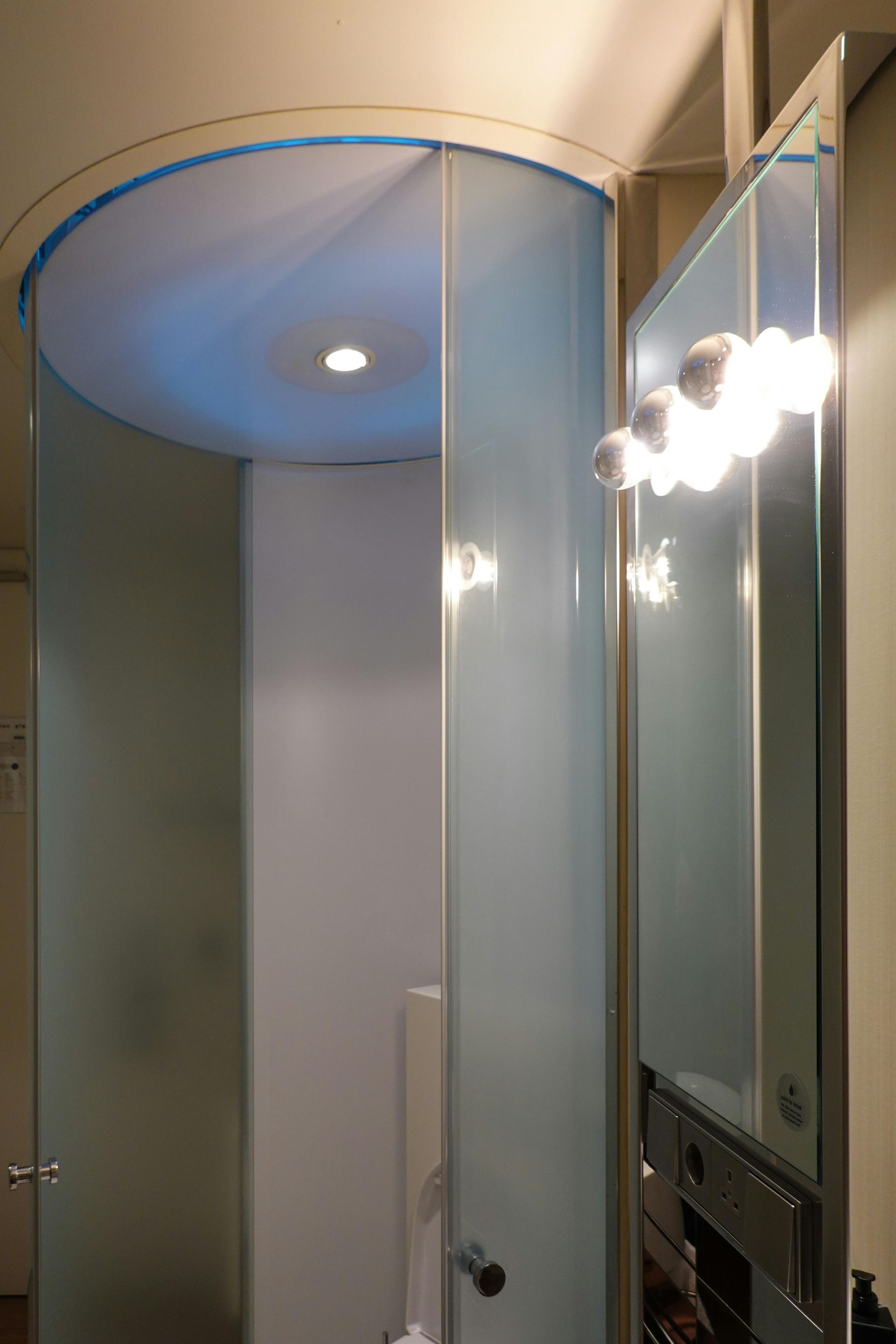 Curved frosted glass shower with blue lighting inside. The door is open, revealing a wall-mounted light fixture.