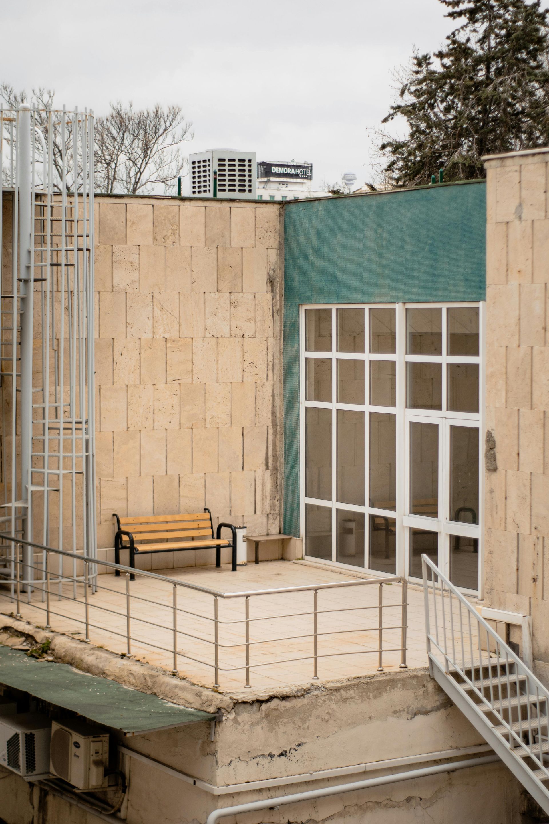 Rooftop seating area with a bench, stairs, and a door, beneath a cloudy sky.