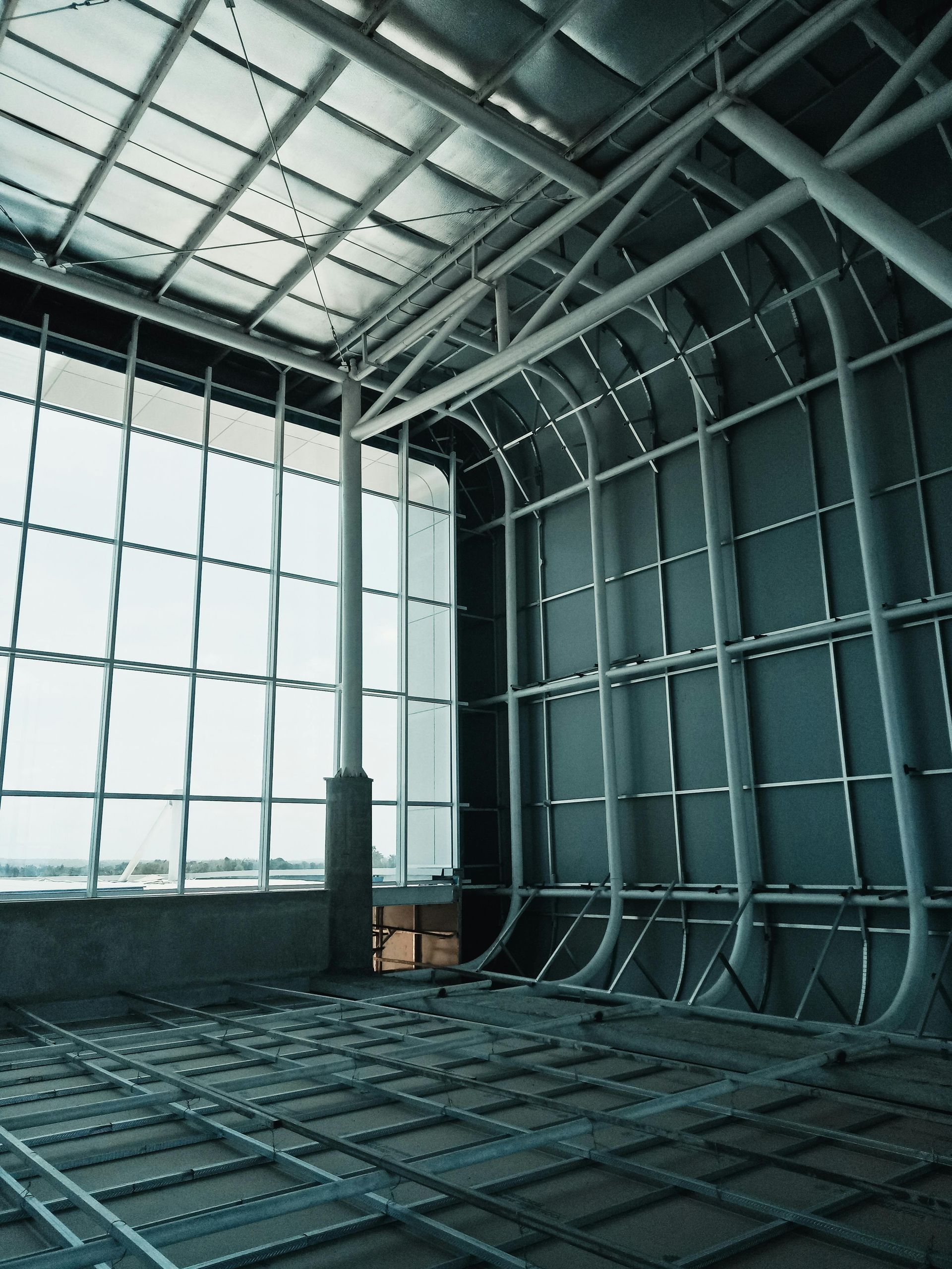 Interior of a building under construction, showing metal framework and large windows.