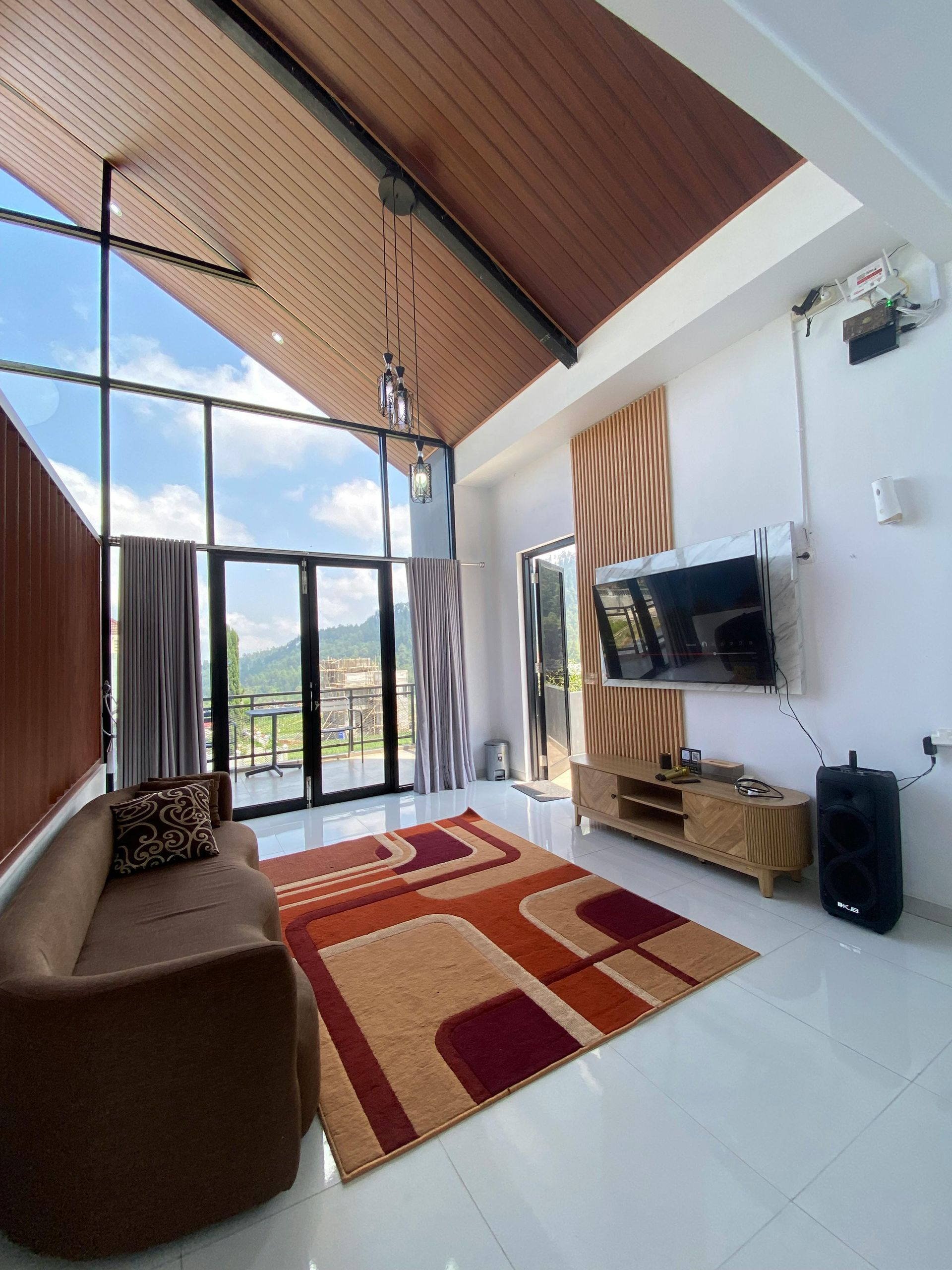 Living room with large windows, mountain view, brown sofa, area rug, tv, and wood ceiling.