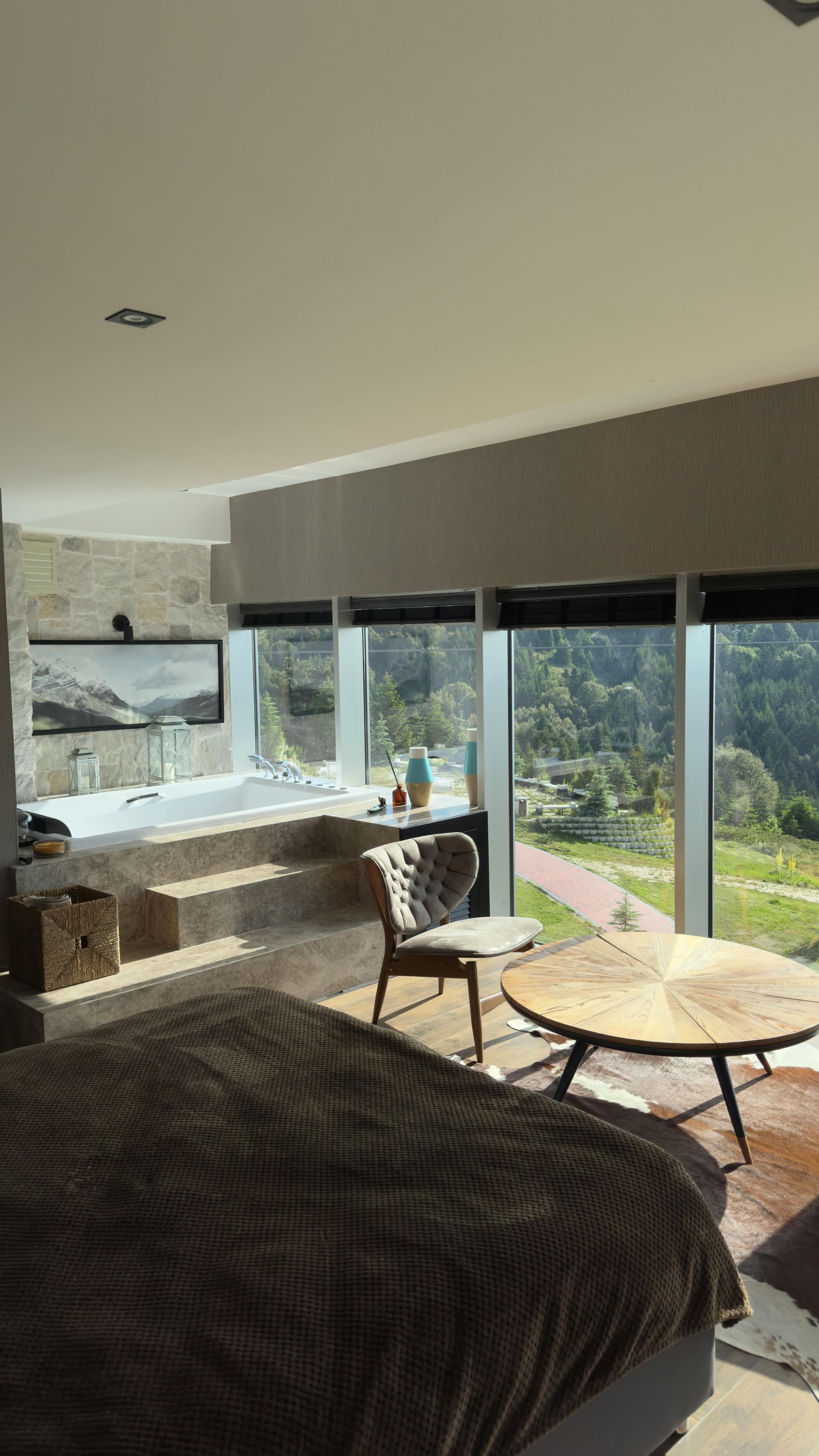 Modern bedroom with built-in jacuzzi and large windows overlooking a green landscape, sunlight streaming in.