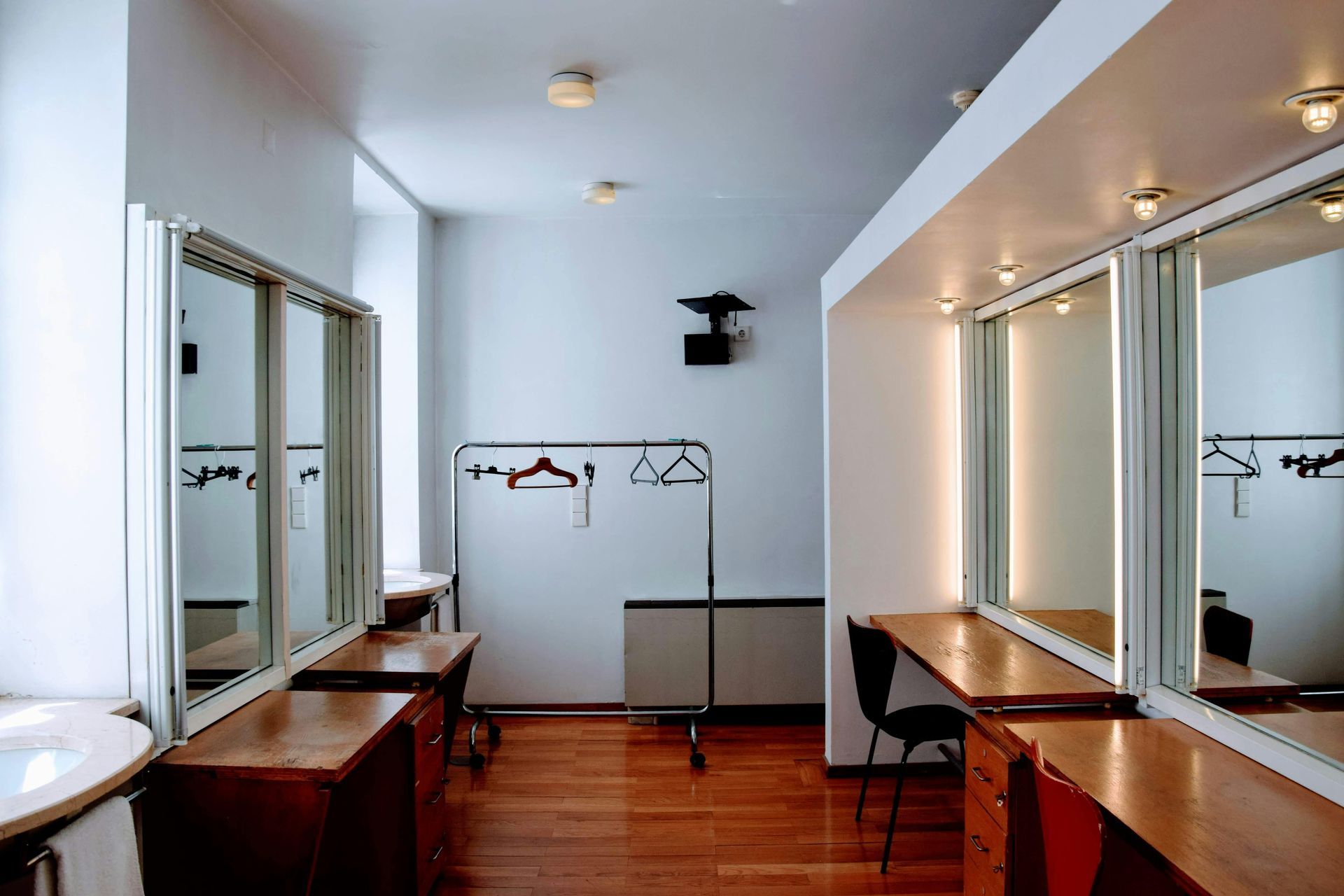 A dressing room with large mirrors, wood counters, and a garment rack.