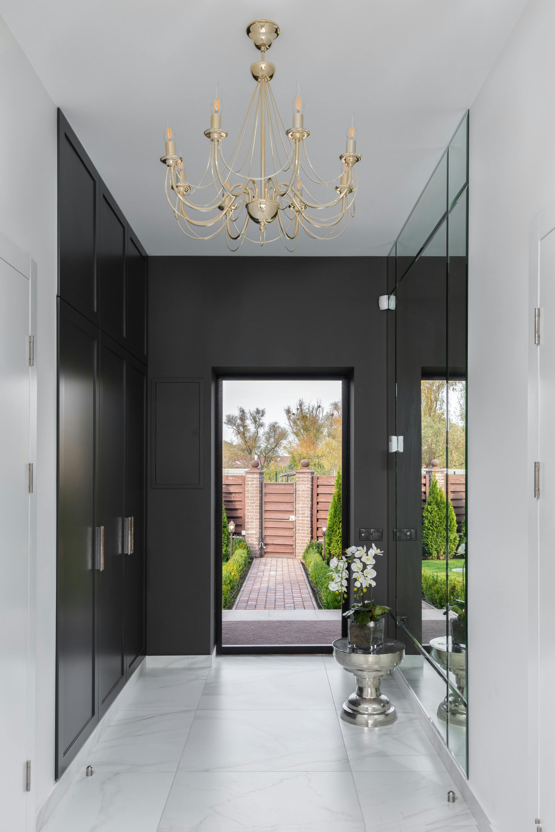 Hallway with black wardrobe, large mirror, and ornate chandelier. View opens to garden.