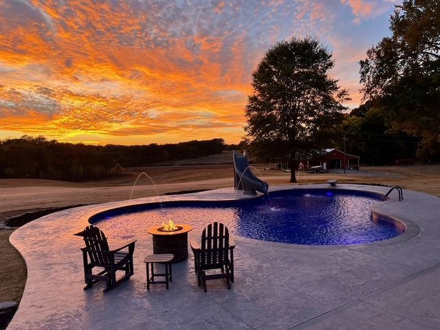 Sunset over a pool with lounge chairs, fire pit, and a water slide.