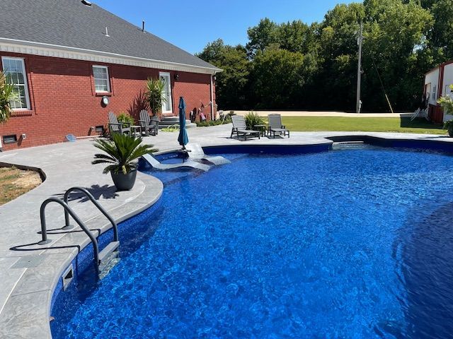 Blue pool with a paved patio next to a red brick house.
