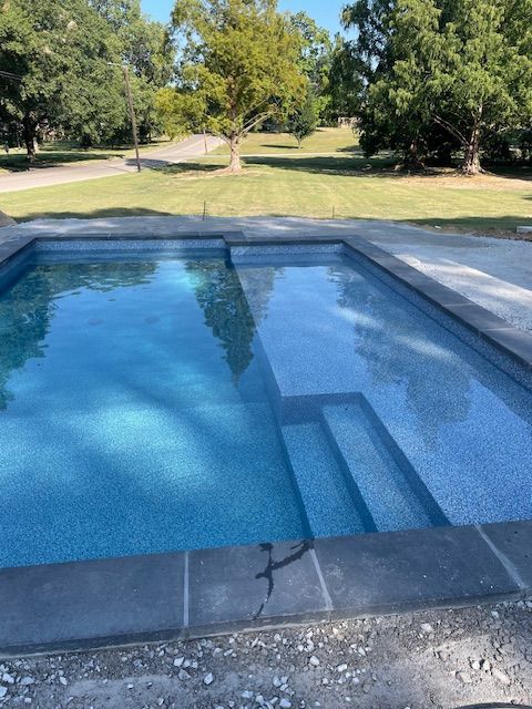 Rectangular swimming pool with steps, filled with water, surrounded by concrete and grass.