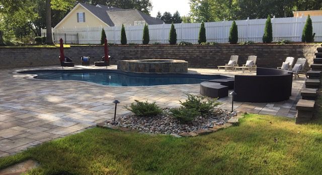 Backyard pool area with a pool, seating, and a fire pit, next to a manicured lawn and white fence.