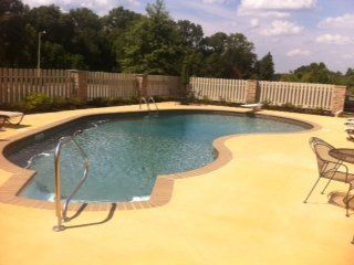 Swimming pool with tan concrete deck and wooden fence.