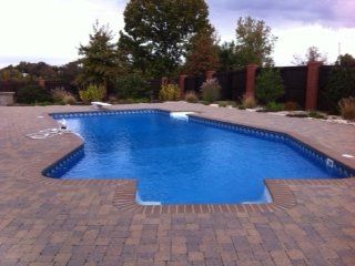 Swimming pool with blue water surrounded by brick patio.