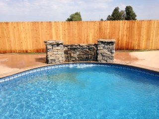 Swimming pool with stone waterfall feature, bordered by a wooden fence.