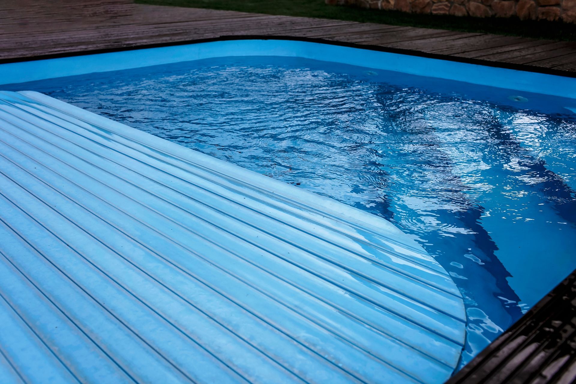 Pool with partial cover, blue water, dark deck, and surrounding greenery.