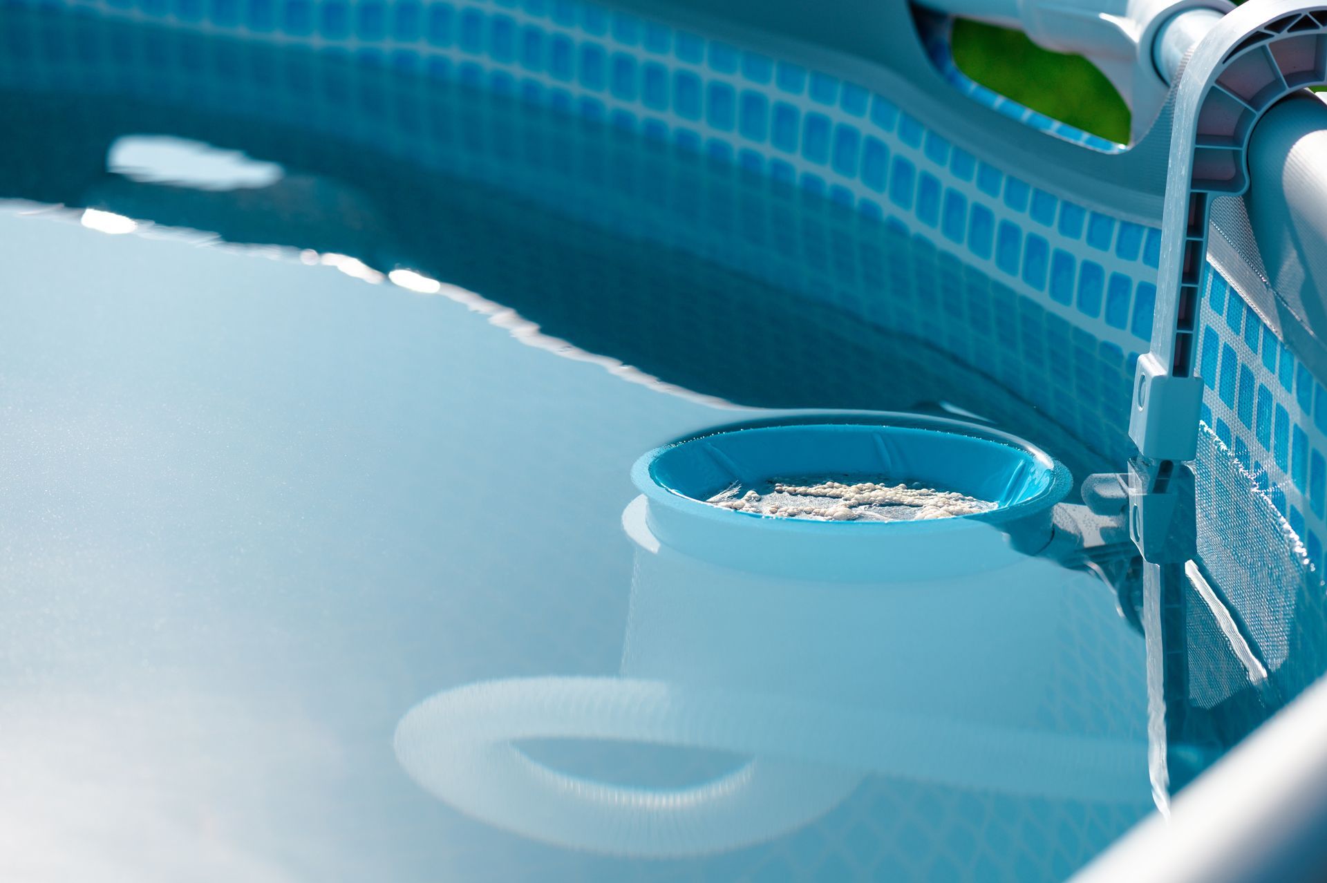 Pool skimmer in a blue tiled above-ground pool, with water and pool equipment visible.