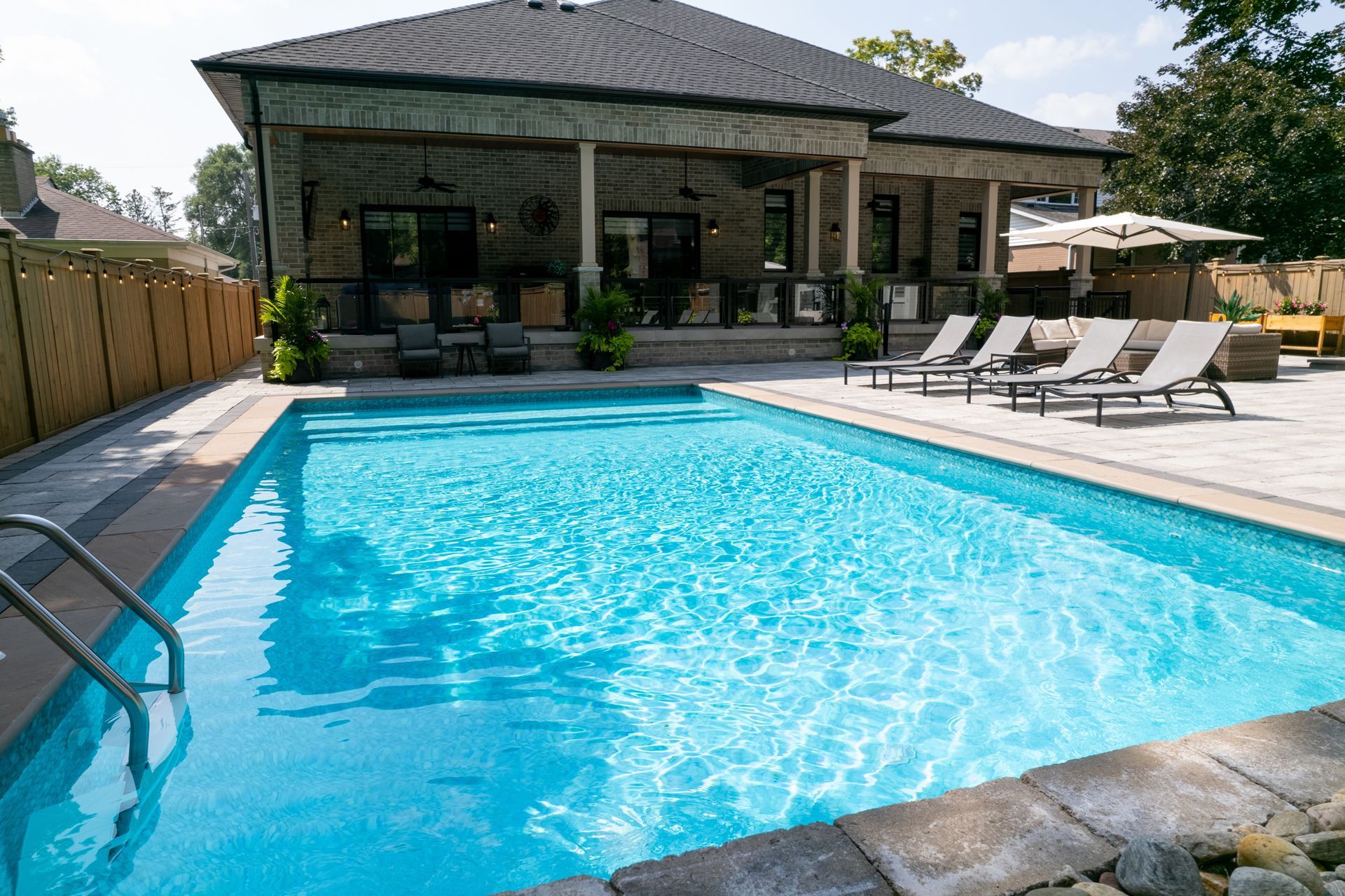 Pool next to a stone house with a covered patio. 
