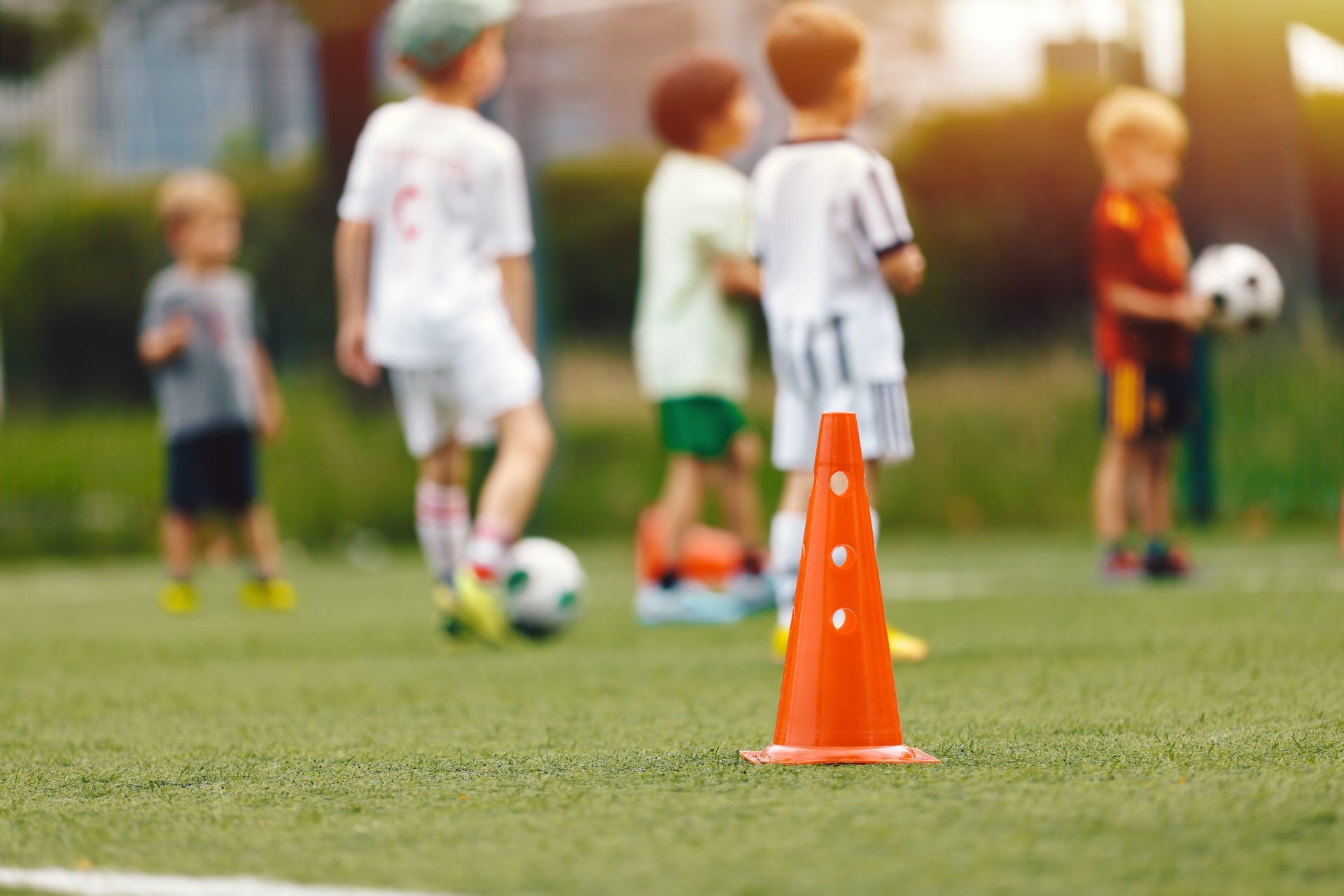 Orange soccer cone on a grassy field with children practicing in the background