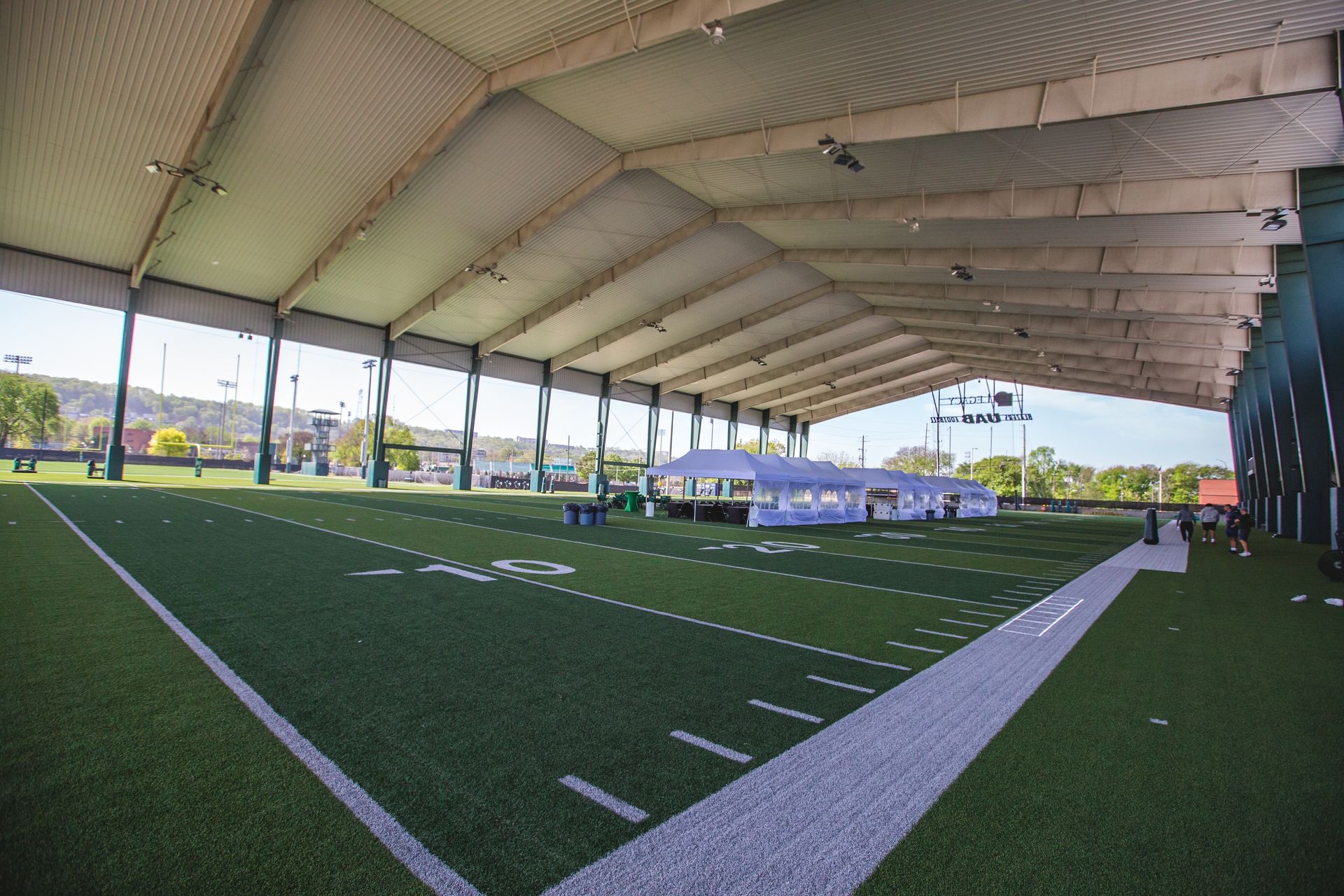 Indoor soccer field with green turf, white lines, and a large covered roof open to the outside