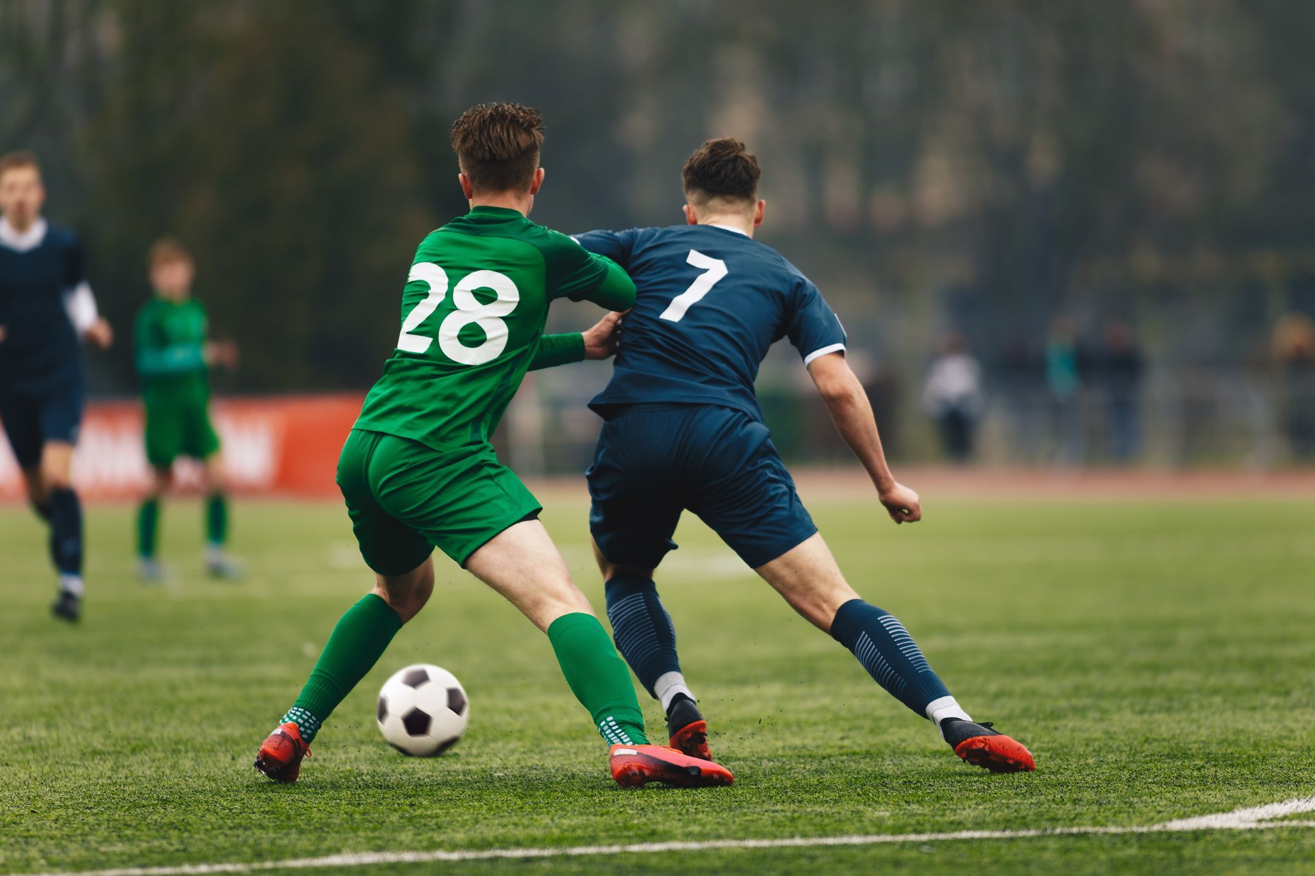 Two soccer players in green and navy vie for the ball on a grassy field