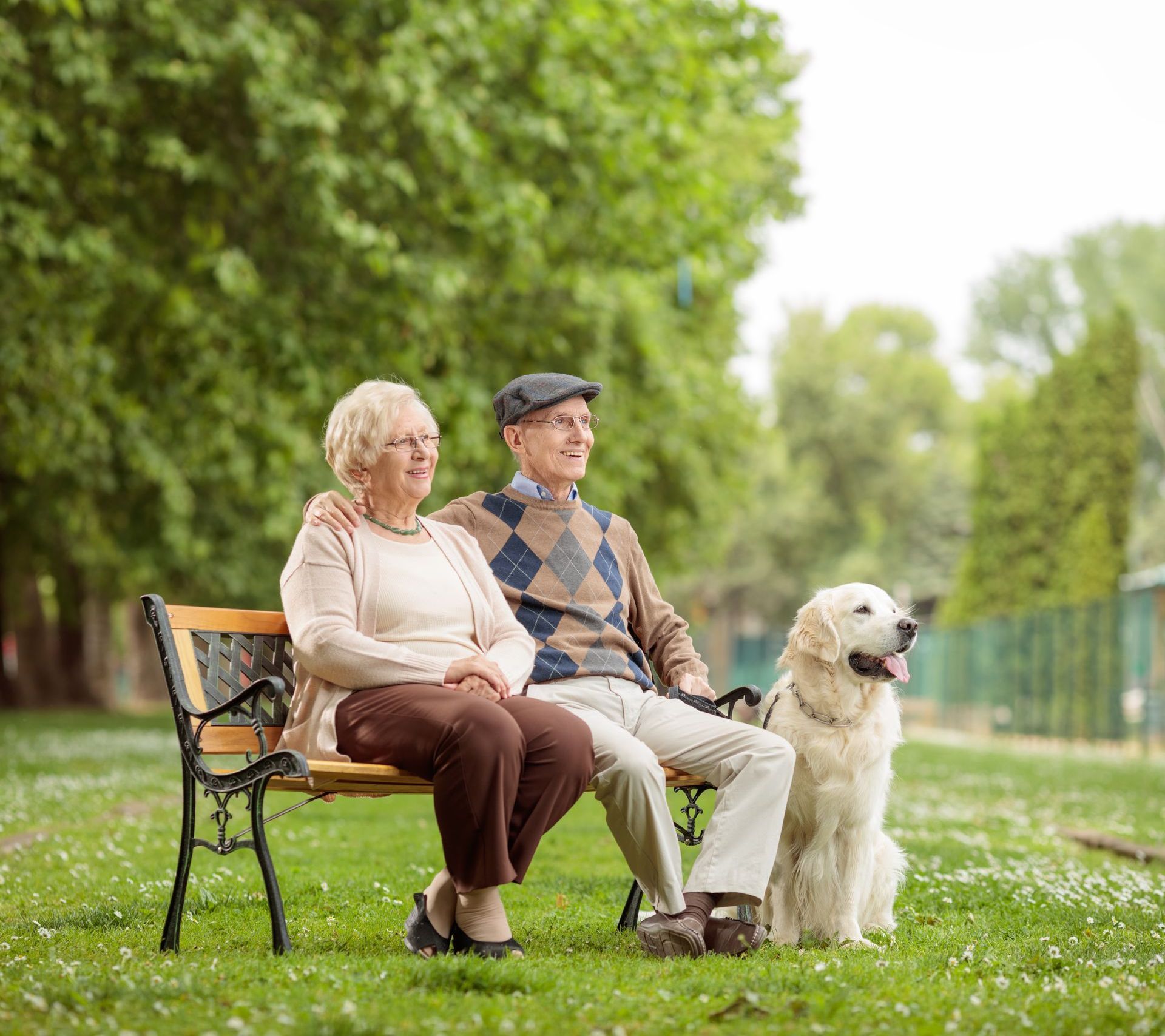 An elderly couple is sitting on a park bench with their dog.