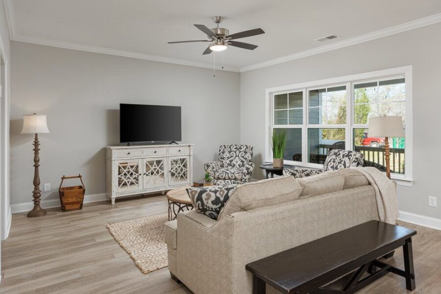 A living room with a couch , chairs , a television and a ceiling fan.