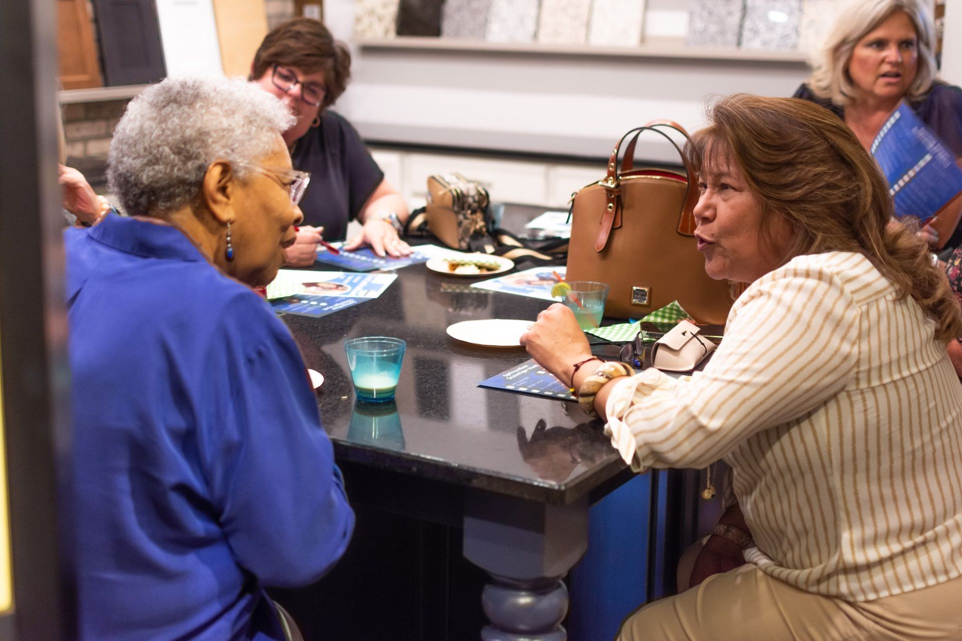A group of women are sitting around a table talking to each other.