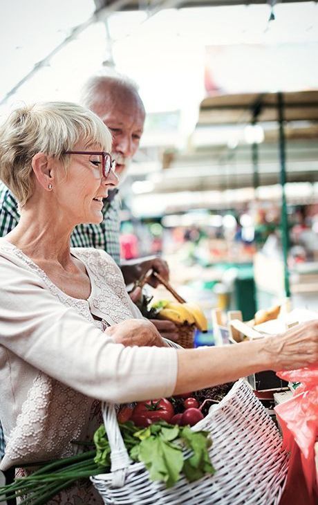 An elderly couple is shopping for vegetables at a market.