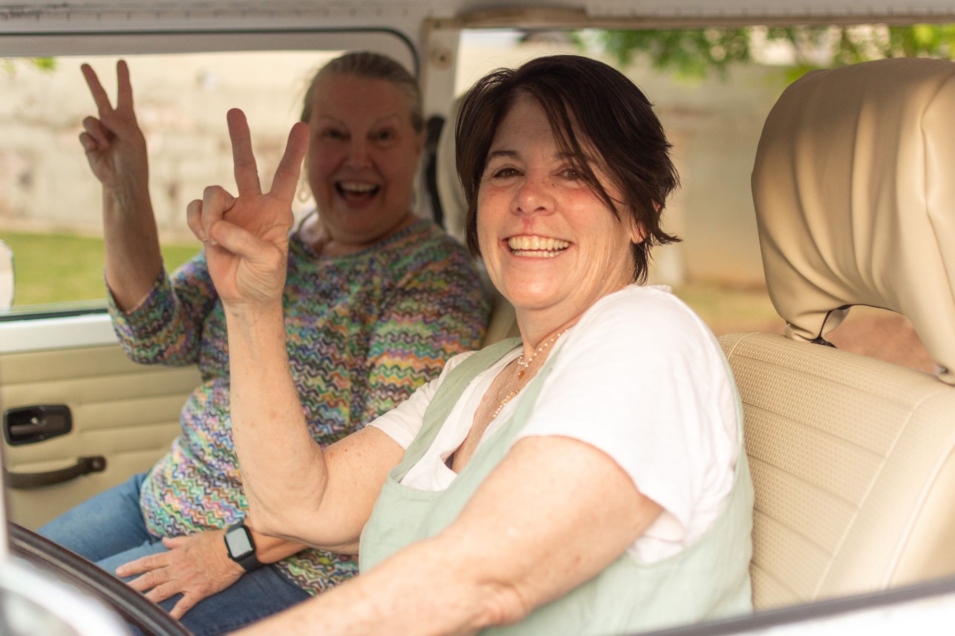 Two women are sitting in the back seat of a car giving a peace sign.