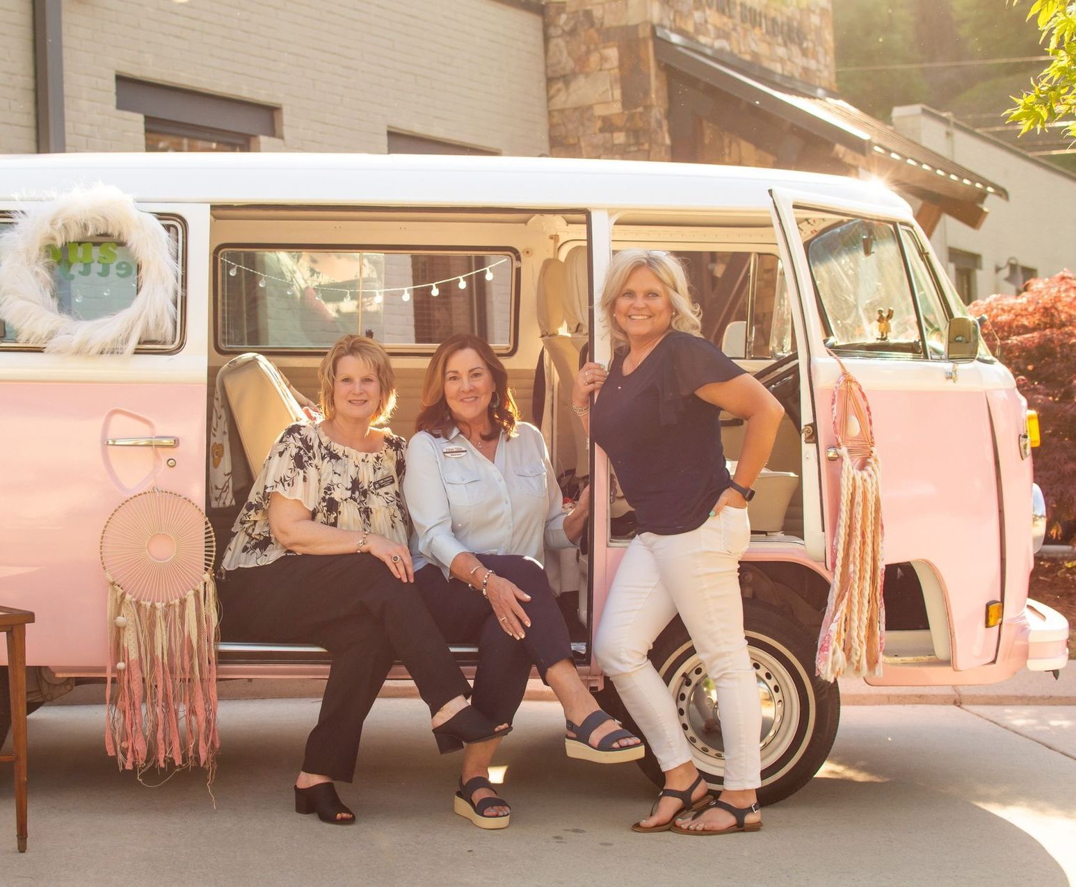 Three women are posing for a picture in front of a pink van.