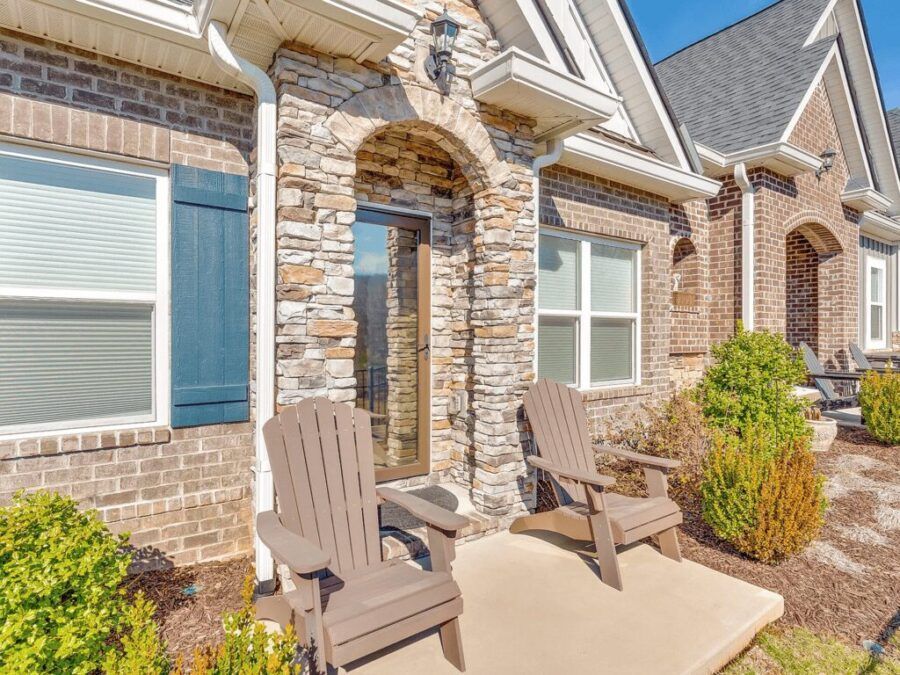 There are two chairs on the porch of a brick house.