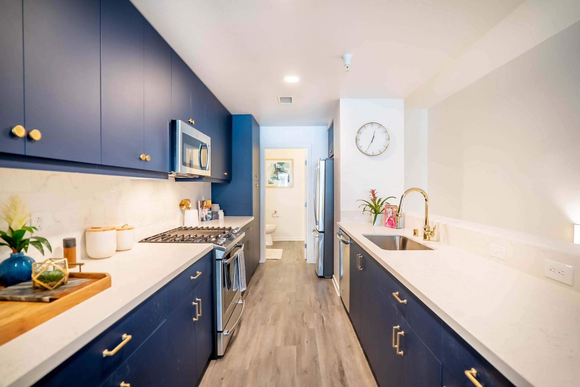 A kitchen with blue cabinets and white counter tops and a clock on the wall.